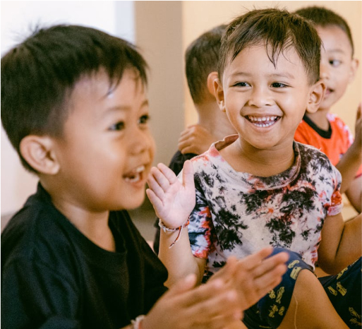 Children smiling and clapping, engaging in joyful play at a community event supporting toy donations for underserved children.